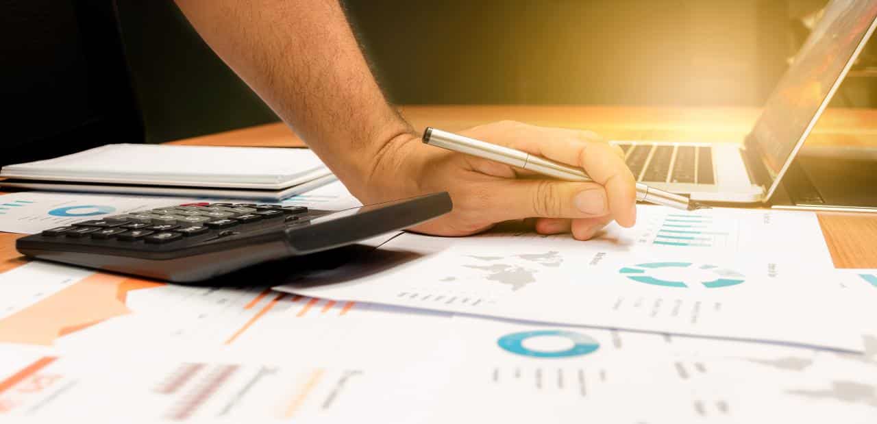 businessman-hand-holding-pen-with-calculator-paperwork-laptop-table-meeting-room